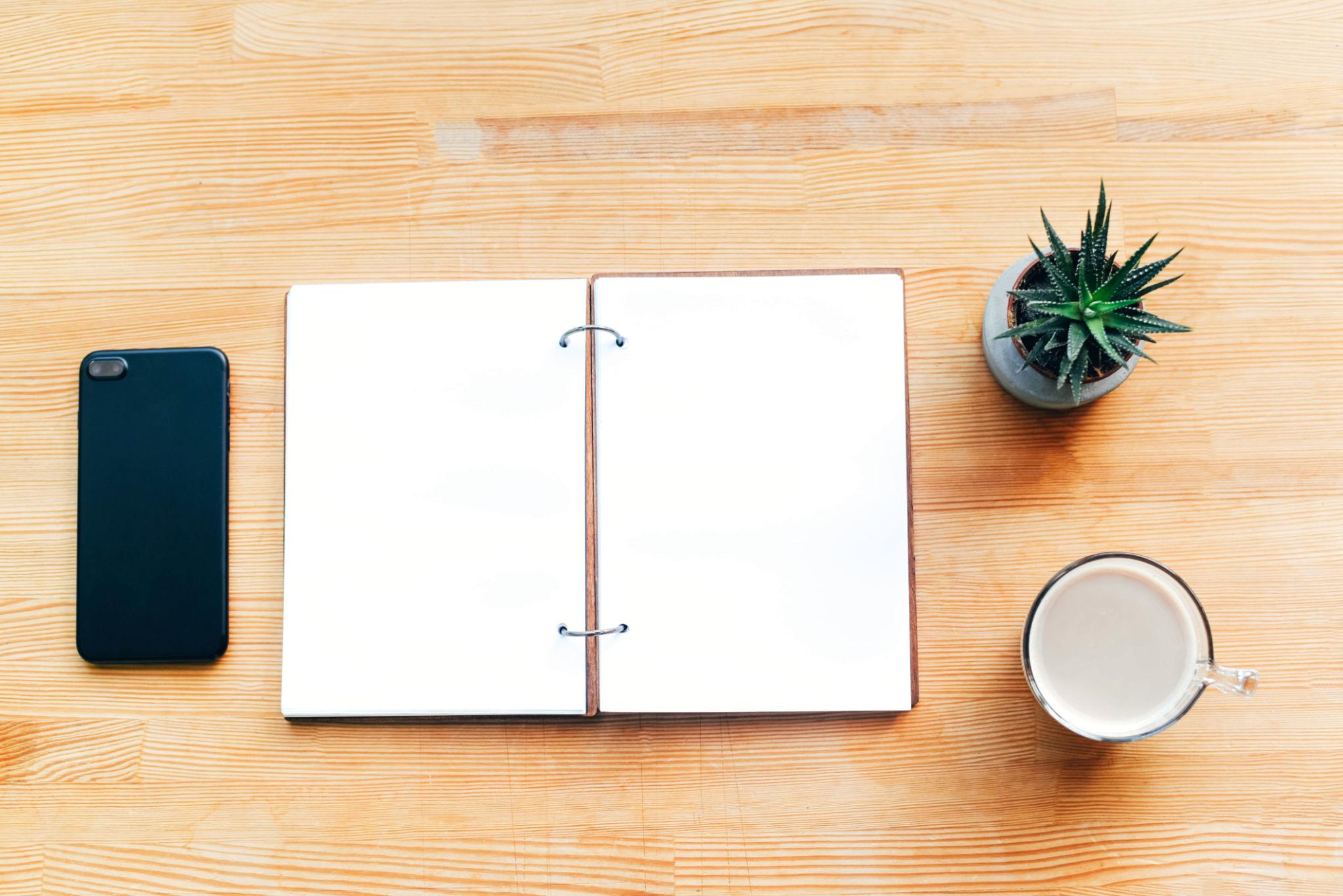 Carnet ouvert sur une table avec téléphone et plante, illustrant un moment de réflexion sur son orientation